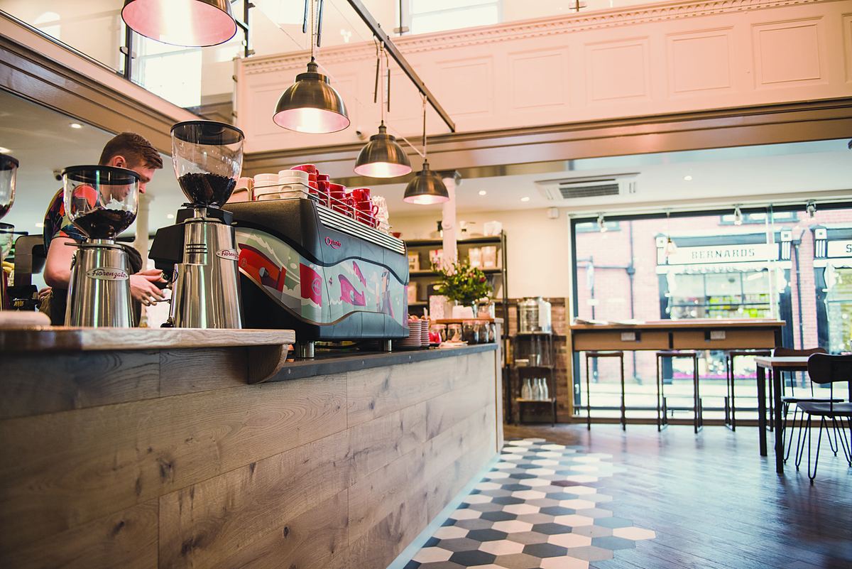 The espresso bar: grinders, a red espresso machine and a barista behind a wooden counter
