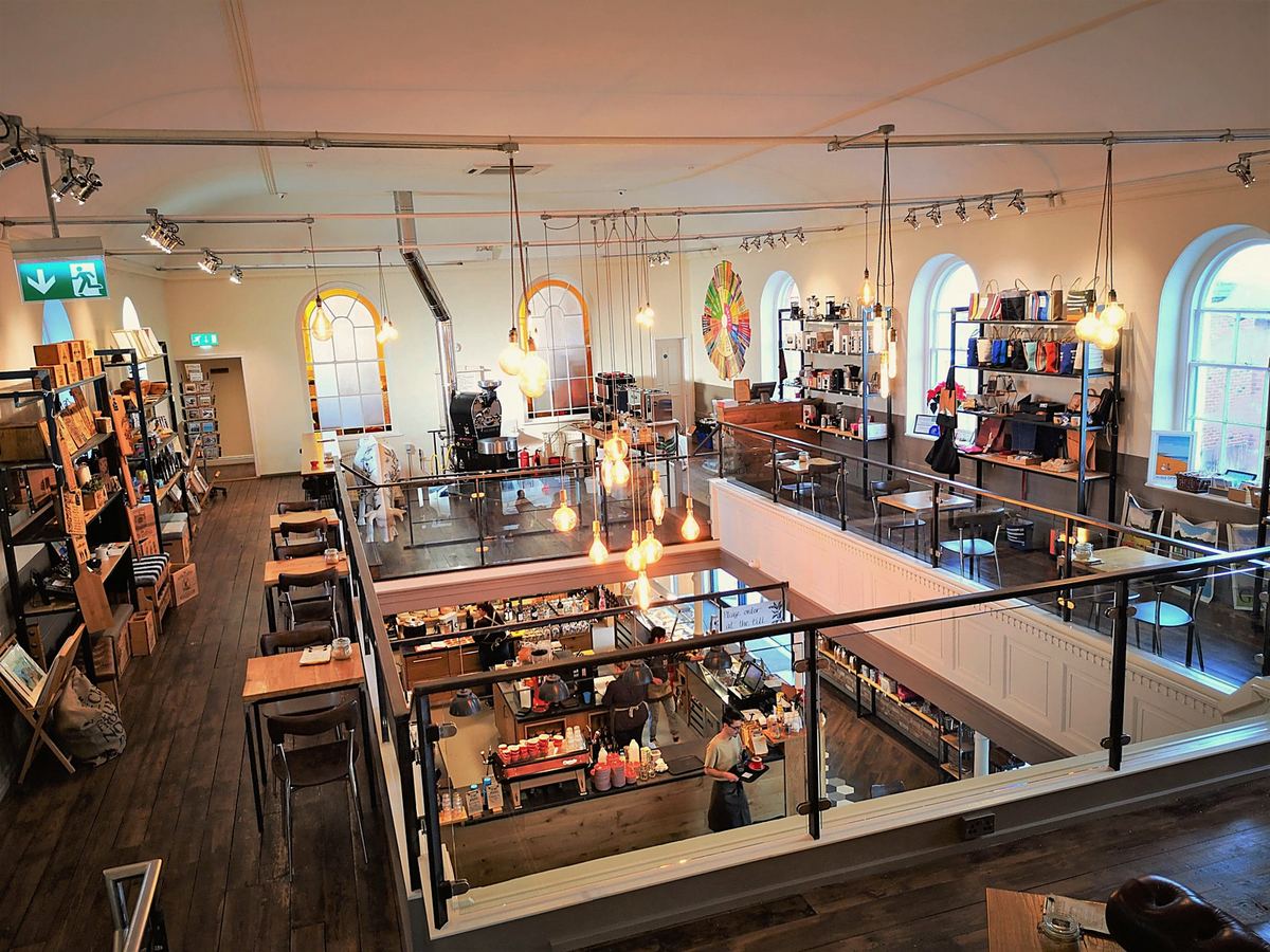 The first floor seen from above: the roaster, shelves of coffee kit and a glass balcony over the café