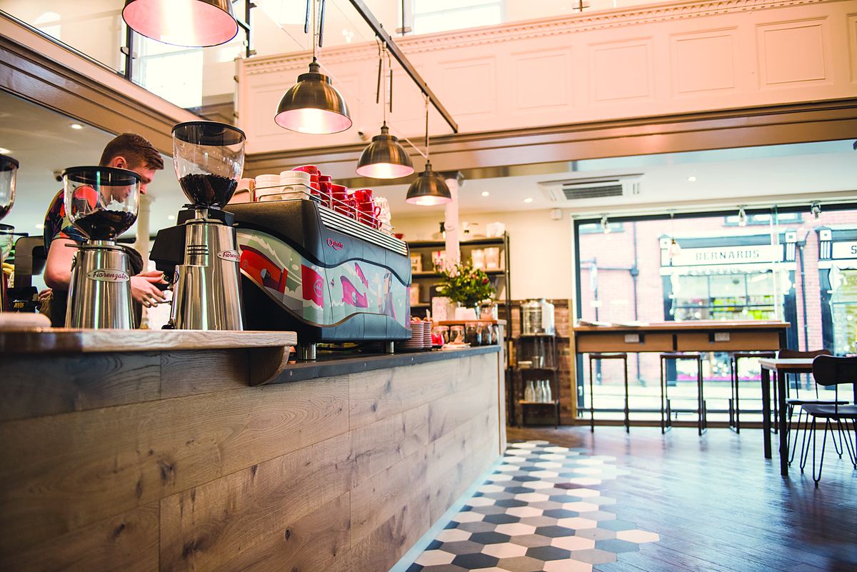 The espresso bar: grinders, a red espresso machine and a barista behind a wooden counter