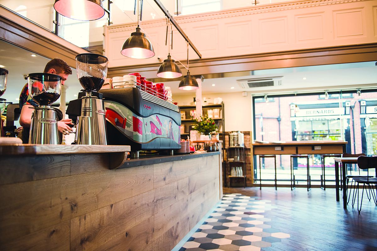 The espresso bar: grinders, a red espresso machine and a barista behind a wooden counter