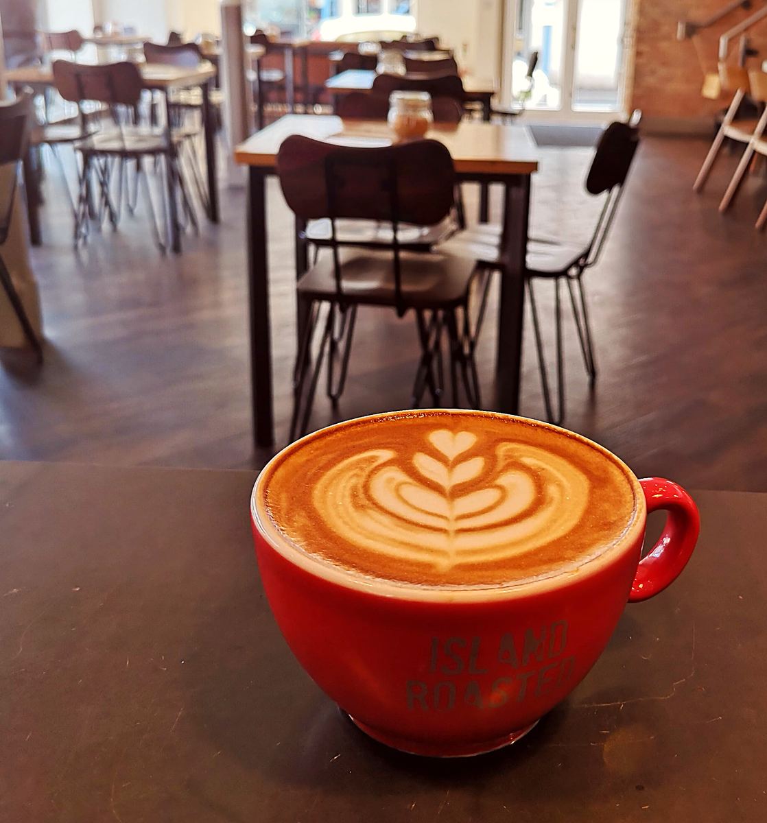 A latte with leaf art in a red cup on a café table