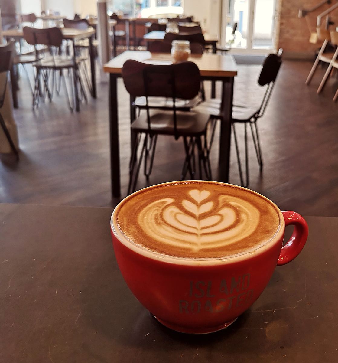 A latte with leaf art in a red cup on a café table
