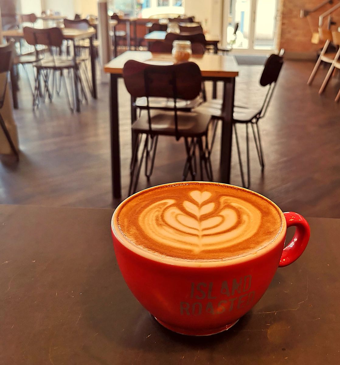 A latte with leaf art in a red cup on a café table
