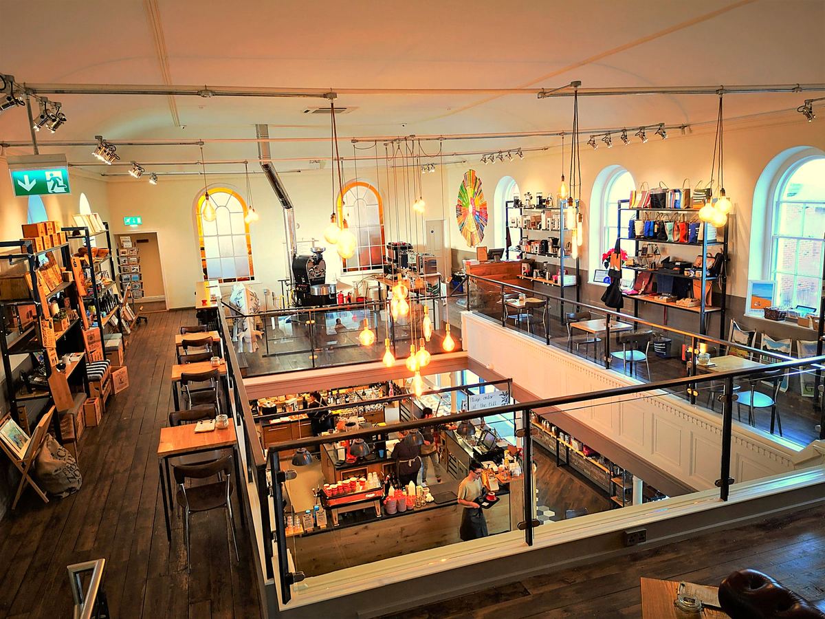 The first floor seen from above: the roaster, shelves of coffee kit and a glass balcony over the café